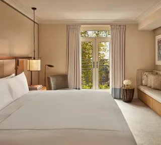 Hotel room with king bed, soft neutral tones, French doors to balcony, and seating area.