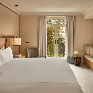 Hotel room with king bed, soft neutral tones, French doors to balcony, and seating area.