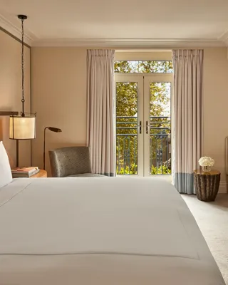 Hotel room with king bed, soft neutral tones, French doors to balcony, and seating area.