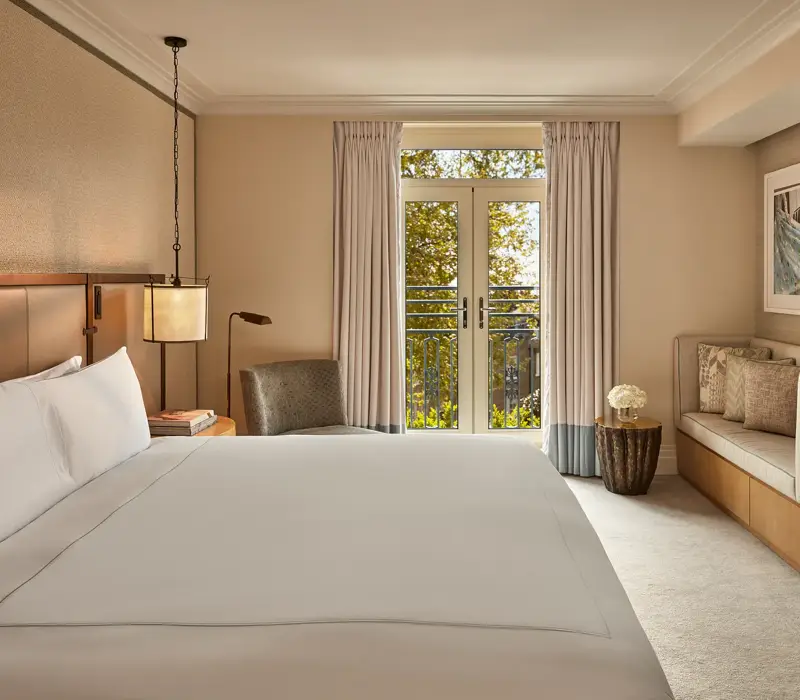 Hotel room with king bed, soft neutral tones, French doors to balcony, and seating area.