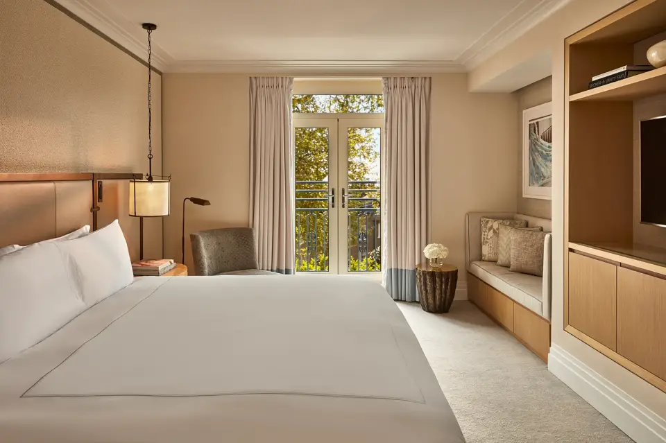 Hotel room with king bed, soft neutral tones, French doors to balcony, and seating area.
