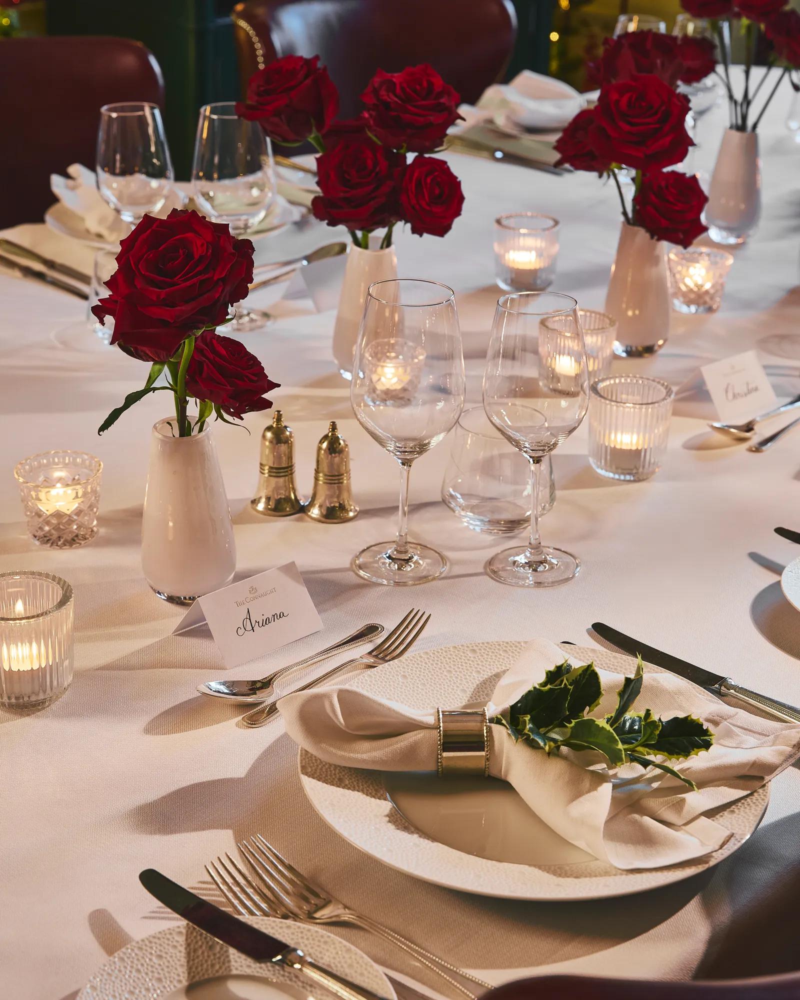 Elegant restaurant table set with white linens, red rose centerpieces, candles, and polished glassware.