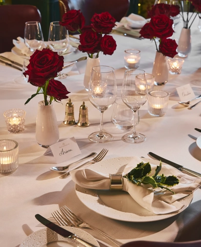 Elegant restaurant table set with white linens, red rose centerpieces, candles, and polished glassware.