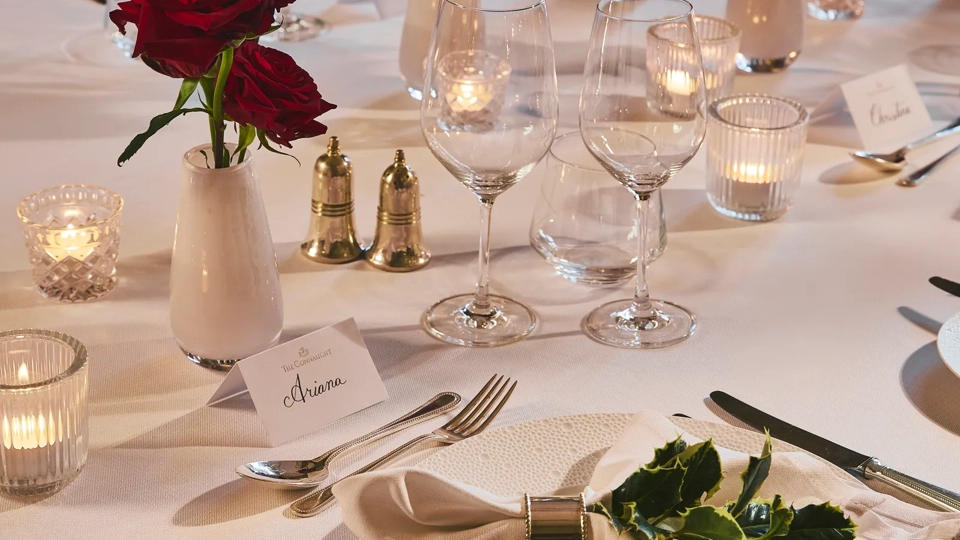 Elegant restaurant table set with white linens, red rose centerpieces, candles, and polished glassware.