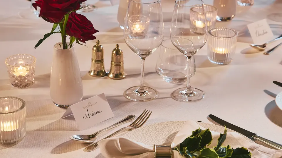 Elegant restaurant table set with white linens, red rose centerpieces, candles, and polished glassware.