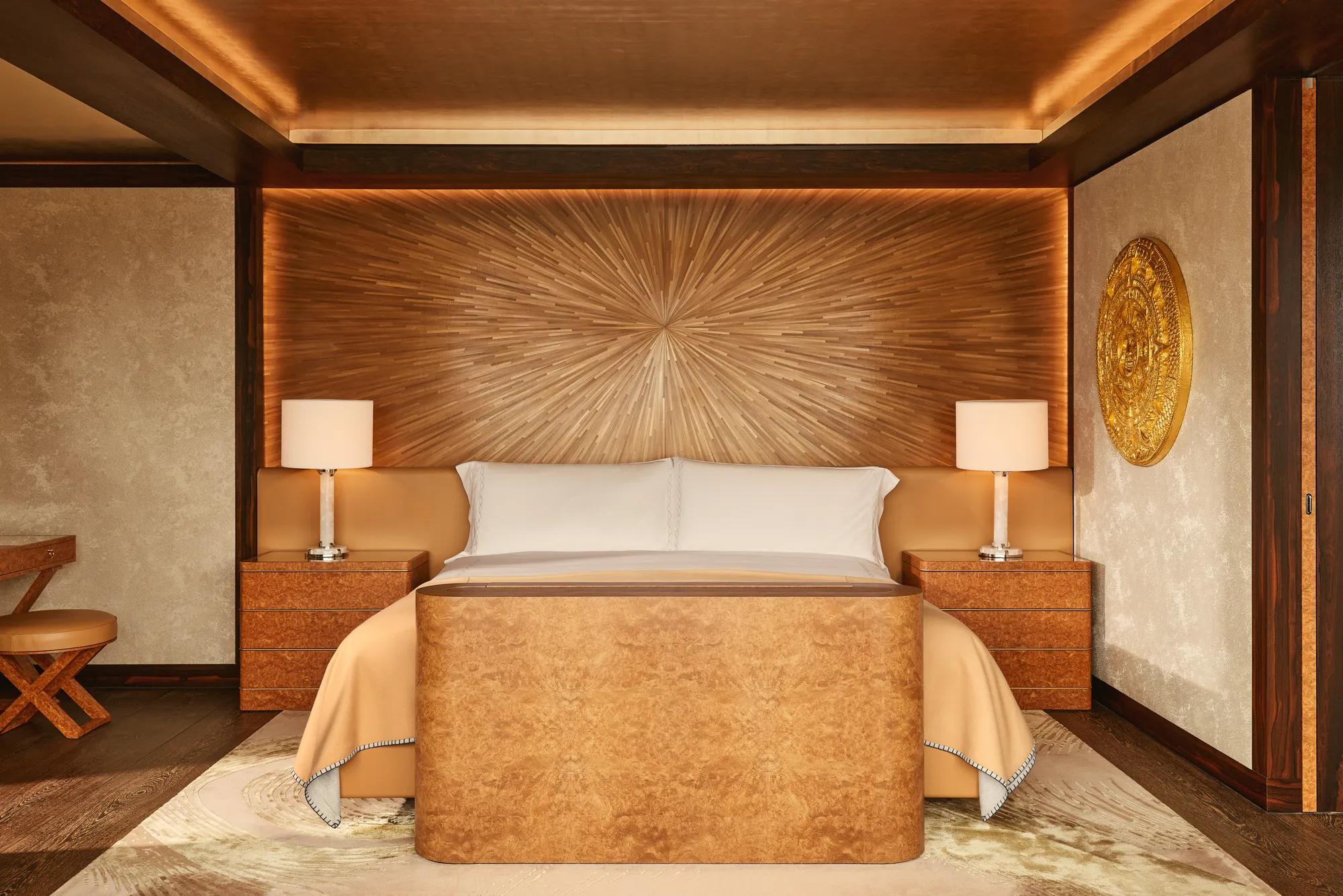 Warm-toned bedroom at Claridge’s with a sunburst wood-panelled headboard, king bed, and amber lighting