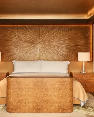 Warm-toned bedroom at Claridge’s with a sunburst wood-panelled headboard, king bed, and amber lighting