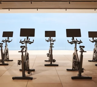 Interior of the Surrenne Riviera open-air fitness studio with a row of indoor exercise bikes positioned on a light-coloured floor, surrounded by natural elements, creating a spacious and airy atmosphere.