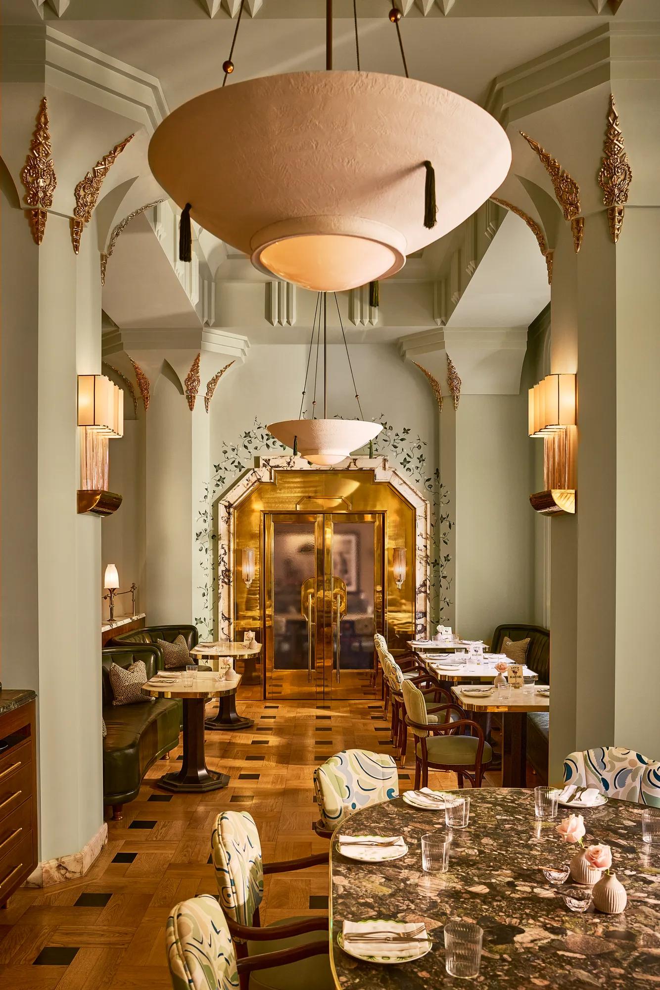 An elegant restaurant interior with Art Deco-inspired arches, sculptural pendant lights, marble tables and gold detailing.