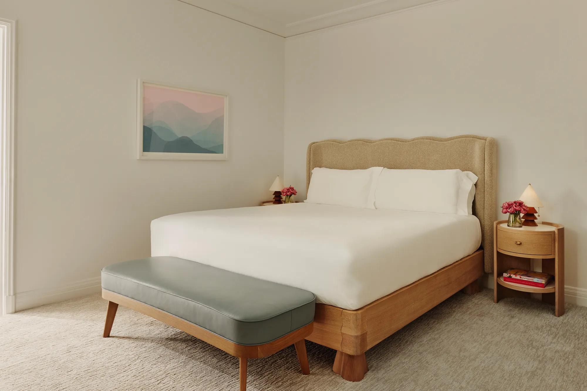 Two-Bedroom Library Suite bedroom with king bed, bench, nightstands, lamps, and pastel artwork in an elegant setting.
