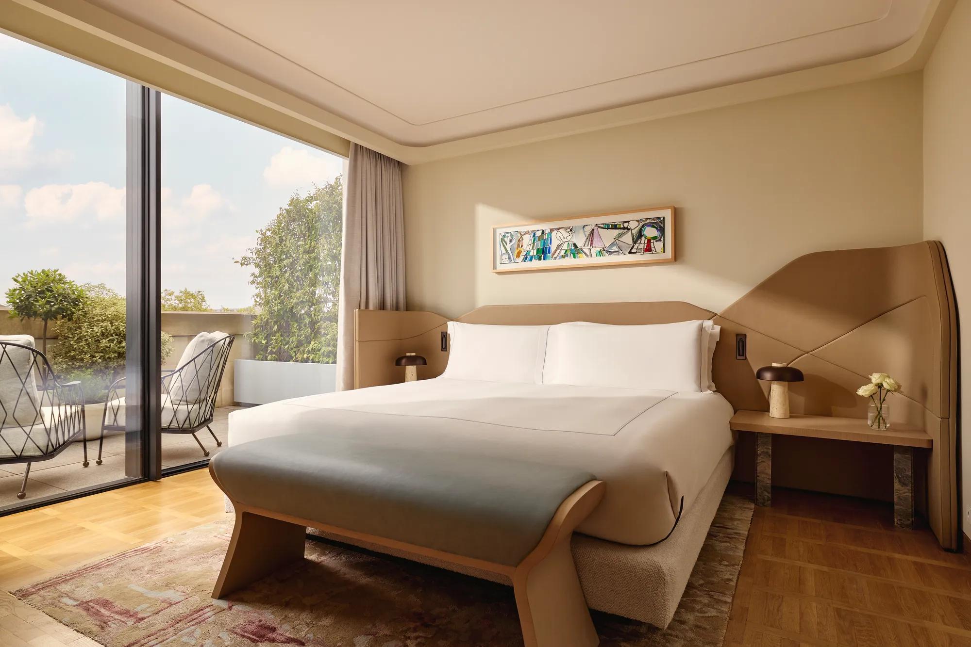 Bedroom with a king-size bed, sculptural tan headboard, and large glass doors leading to a private terrace.