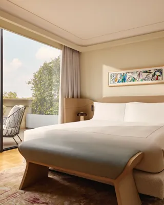 Bedroom with a king-size bed, sculptural tan headboard, and large glass doors leading to a private terrace.