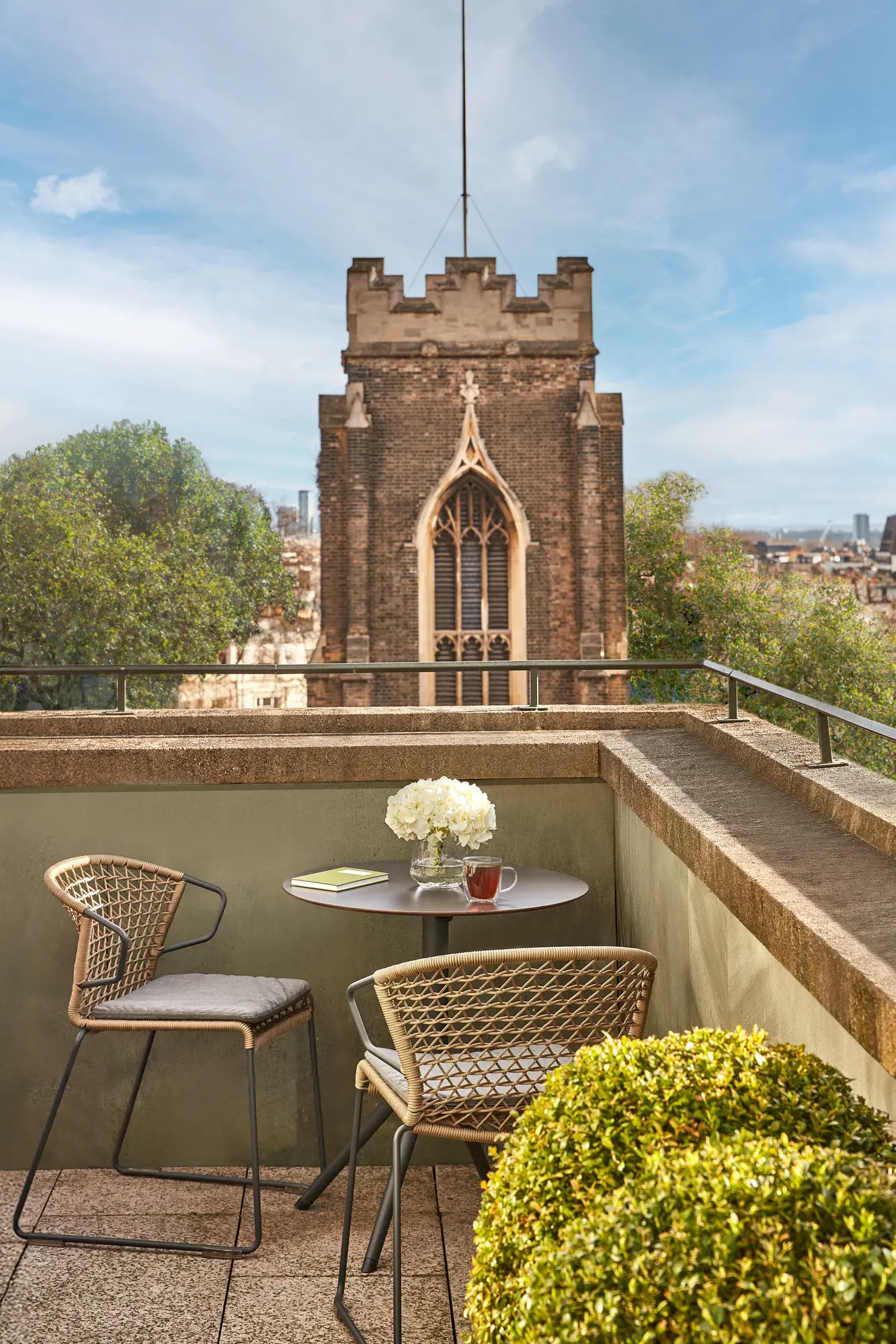 Terrace with round table, chairs, flowers, and city view featuring historic church tower.