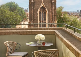 Terrace with round table, chairs, flowers, and city view featuring historic church tower.
