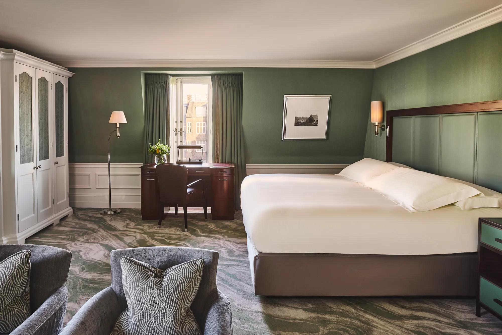 Spacious guest room with king bed, green walls, desk by window, and two armchairs.
