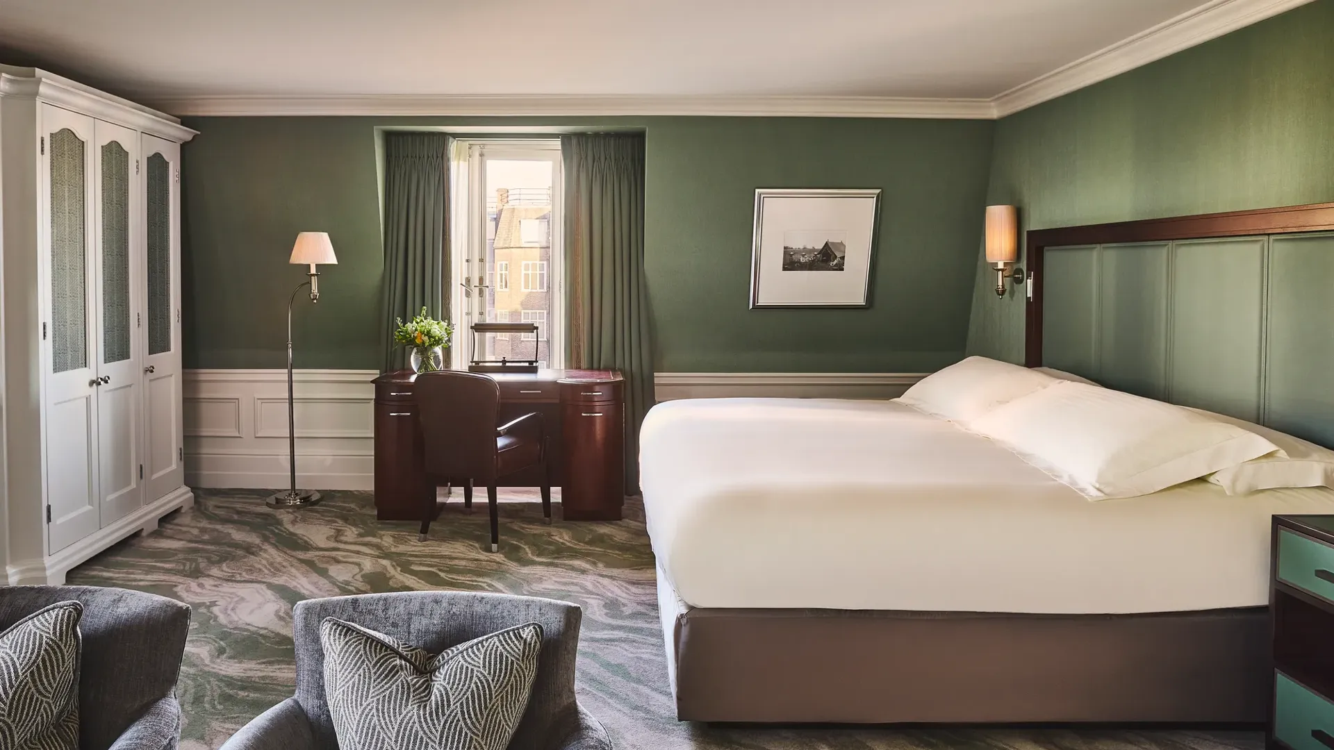 Spacious guest room with king bed, green walls, desk by window, and two armchairs.