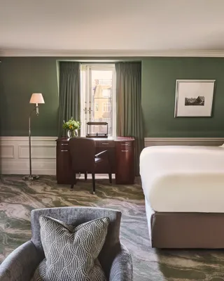 Spacious guest room with king bed, green walls, desk by window, and two armchairs.