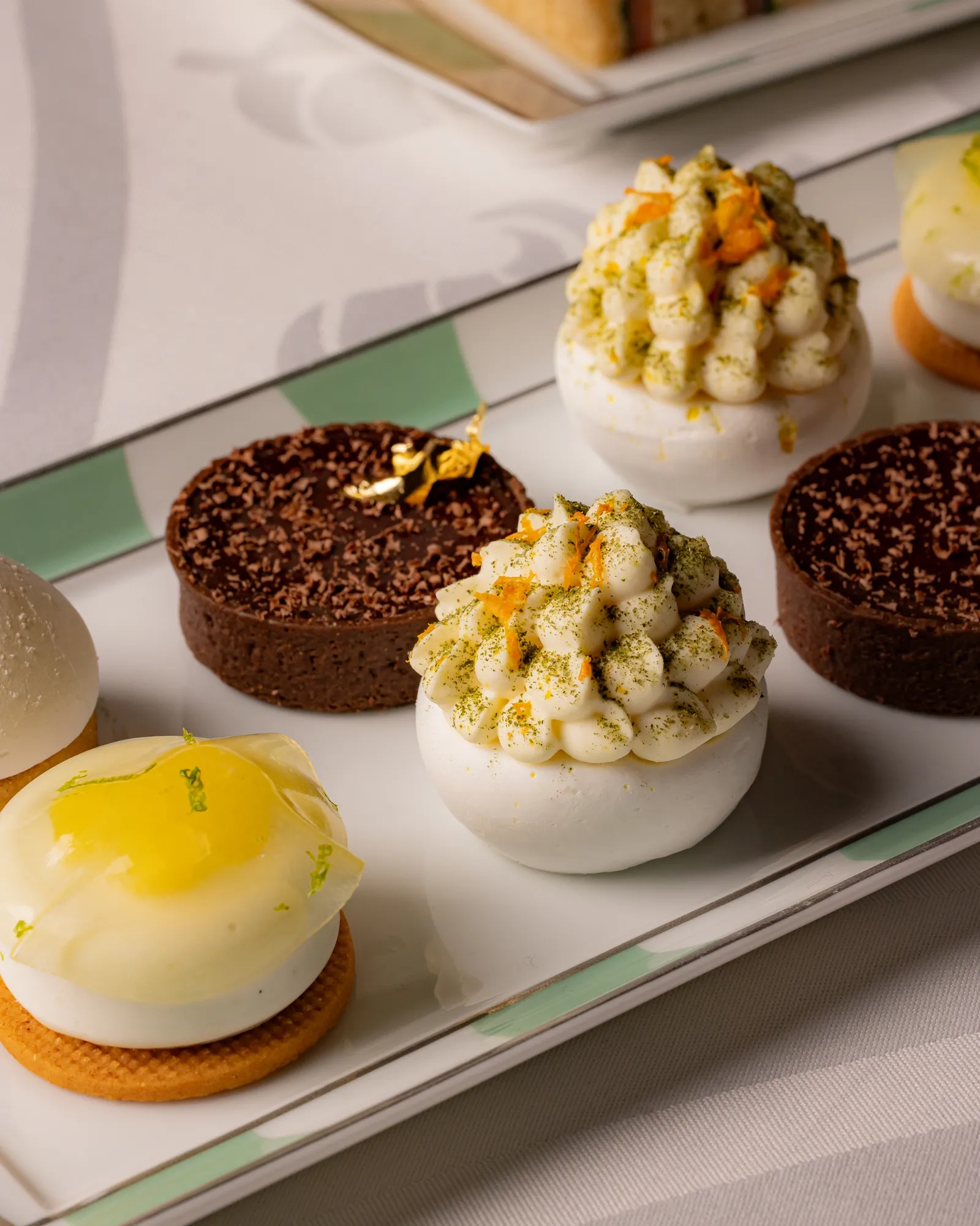 Assorted miniature pastries with citrus, cream and chocolate toppings on a striped platter.