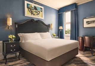 Elegant bedroom with a dark wood bed frame, crisp white bedding, blue walls and curtains, and matching bedside tables with flowers.