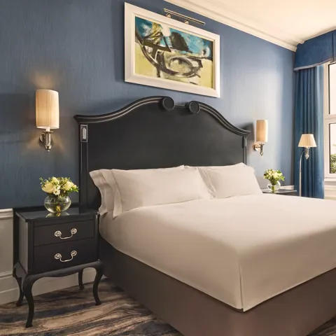 Elegant bedroom with a dark wood bed frame, crisp white bedding, blue walls and curtains, and matching bedside tables with flowers.