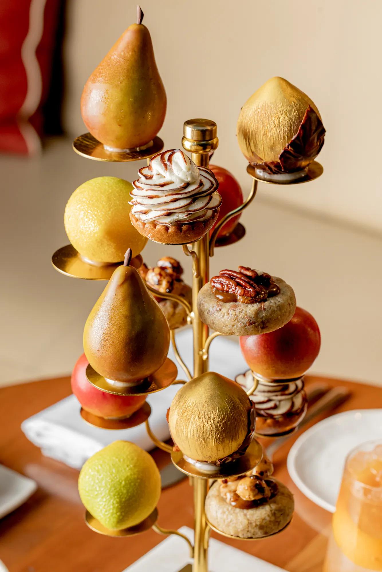 Fruit-inspired pastries and whole fruits displayed on a decorative afternoon tea stand.