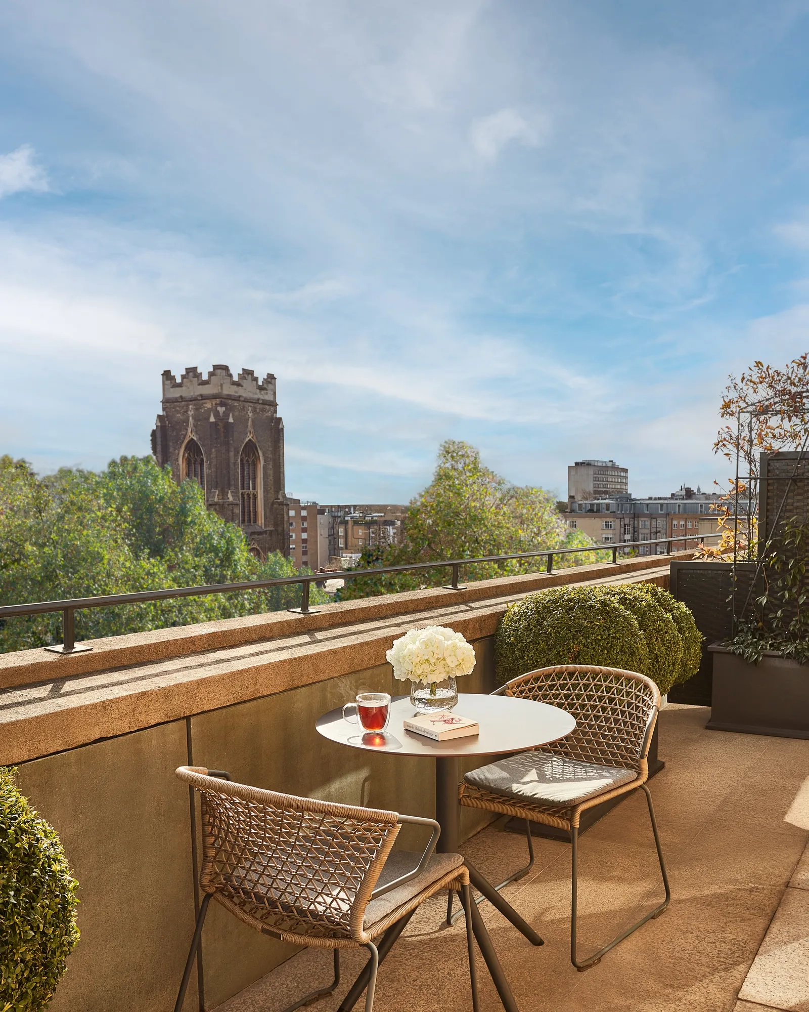 Balcony with table, chairs, white flowers, and city view including a historic church tower.