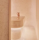 Minimalist spa steam room with smooth, curved beige stone walls and a central stone table topped with a copper water jug.