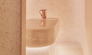 Minimalist spa steam room with smooth, curved beige stone walls and a central stone table topped with a copper water jug.