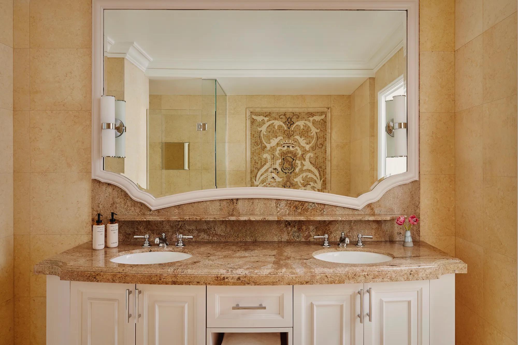 Two-Bedroom Library Suite bathroom with marble countertop, double vanity, twin sinks, large mirror, and decorative stone wall panel.
