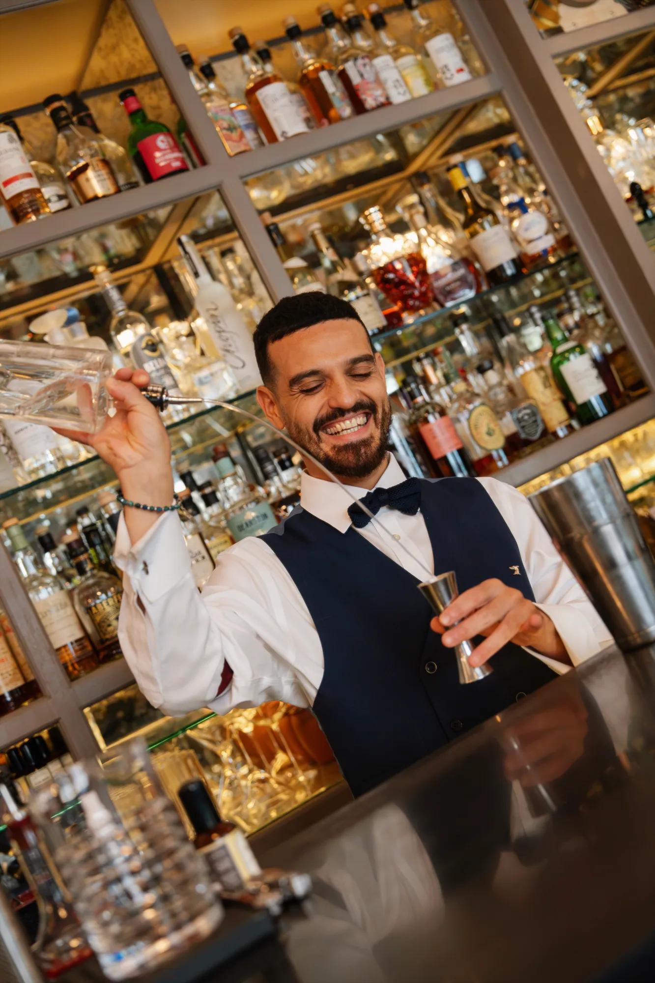 Bartender preparing a cocktail behind a mirrored back bar lined with premium spirits and glassware.