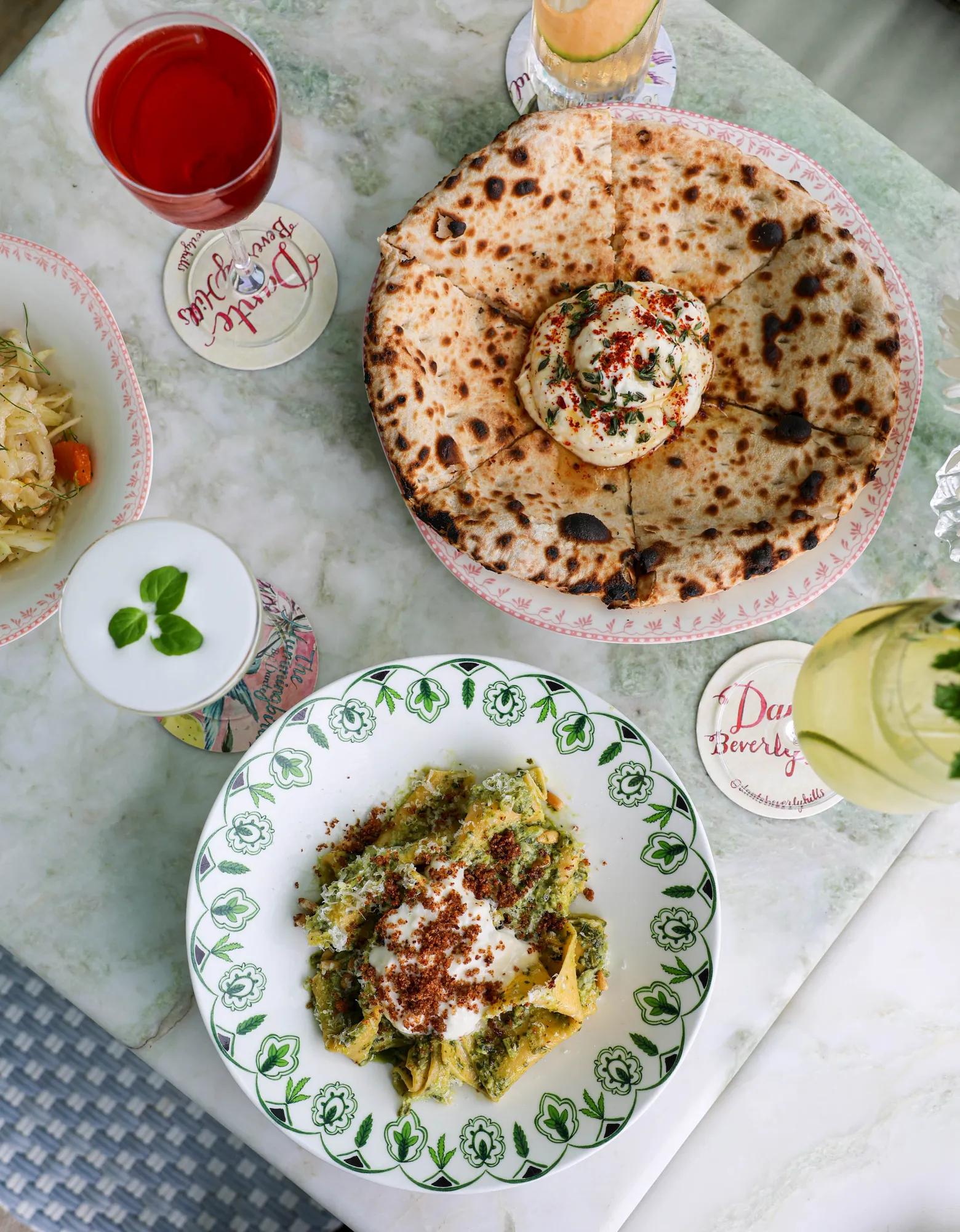 Table with flatbread, pasta dish, and assorted cocktails at Dante Beverly Hills.