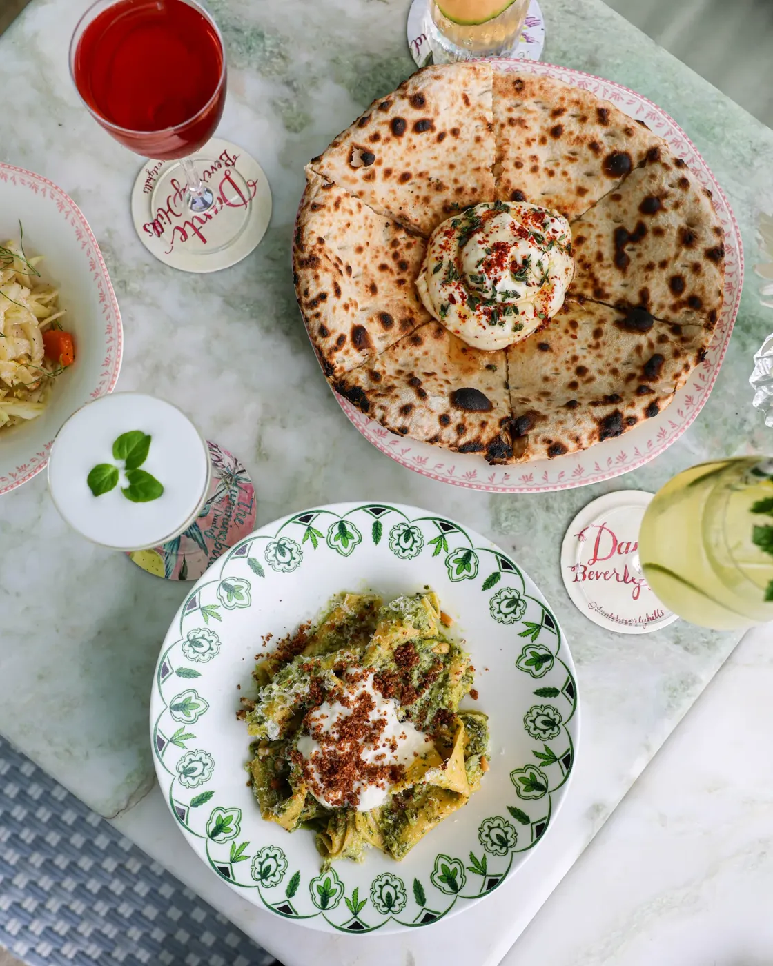 Table with flatbread, pasta dish, and assorted cocktails at Dante Beverly Hills.