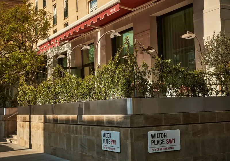 Street view of a building with a red awning and greenery along a raised terrace on Wilton Place in Westminster.