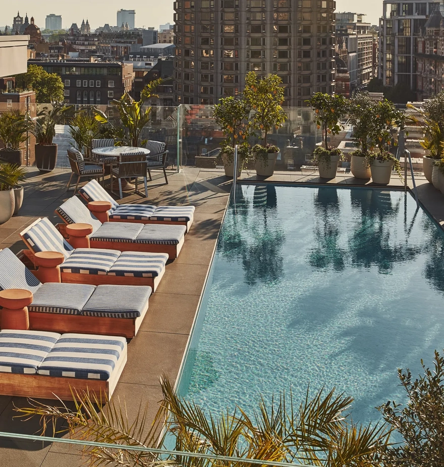 Rooftop pool with striped loungers, bar seating, greenery, and city skyline views.