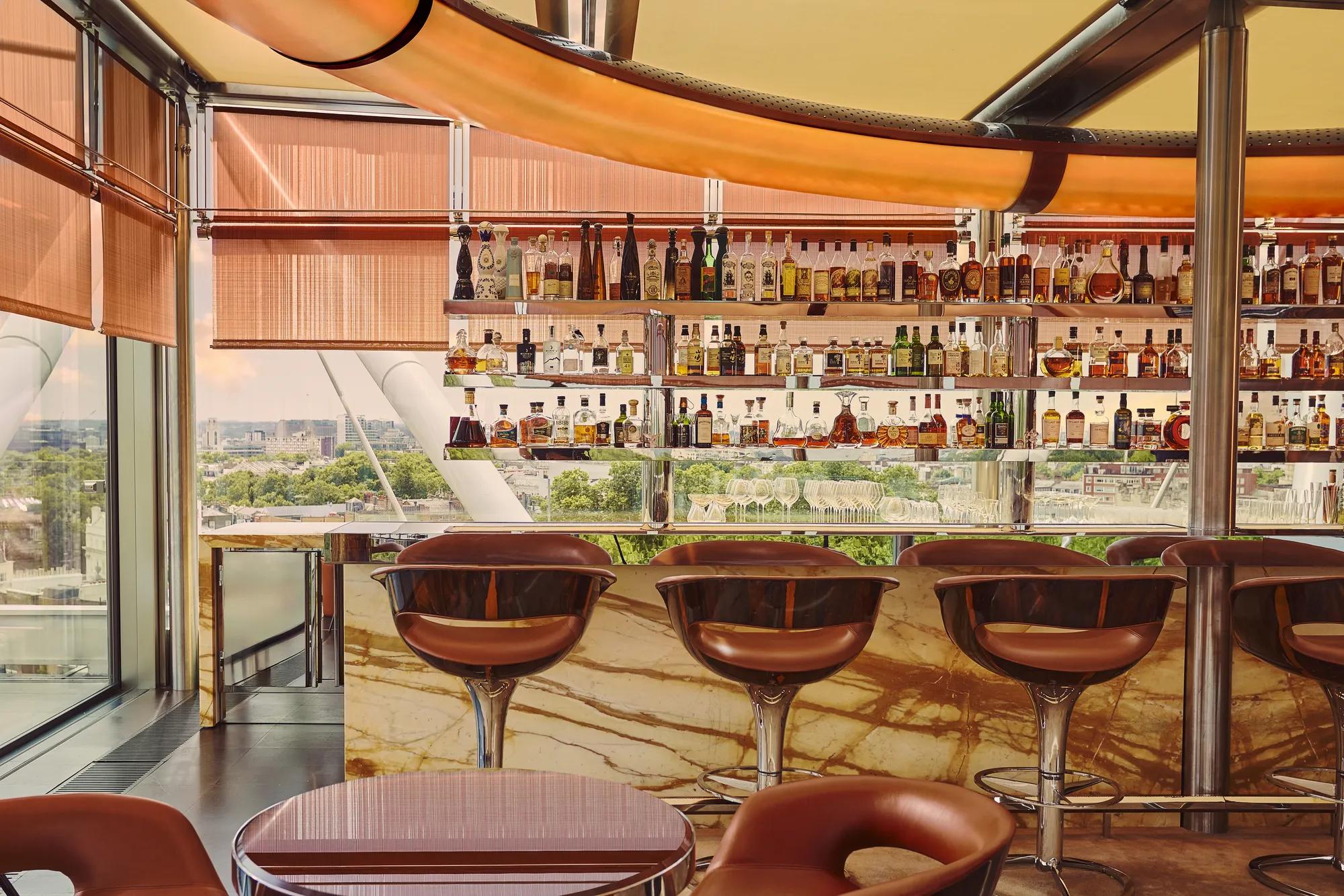 A stylish bar with marble counters, leather stools, and a panoramic city view through floor-to-ceiling windows.