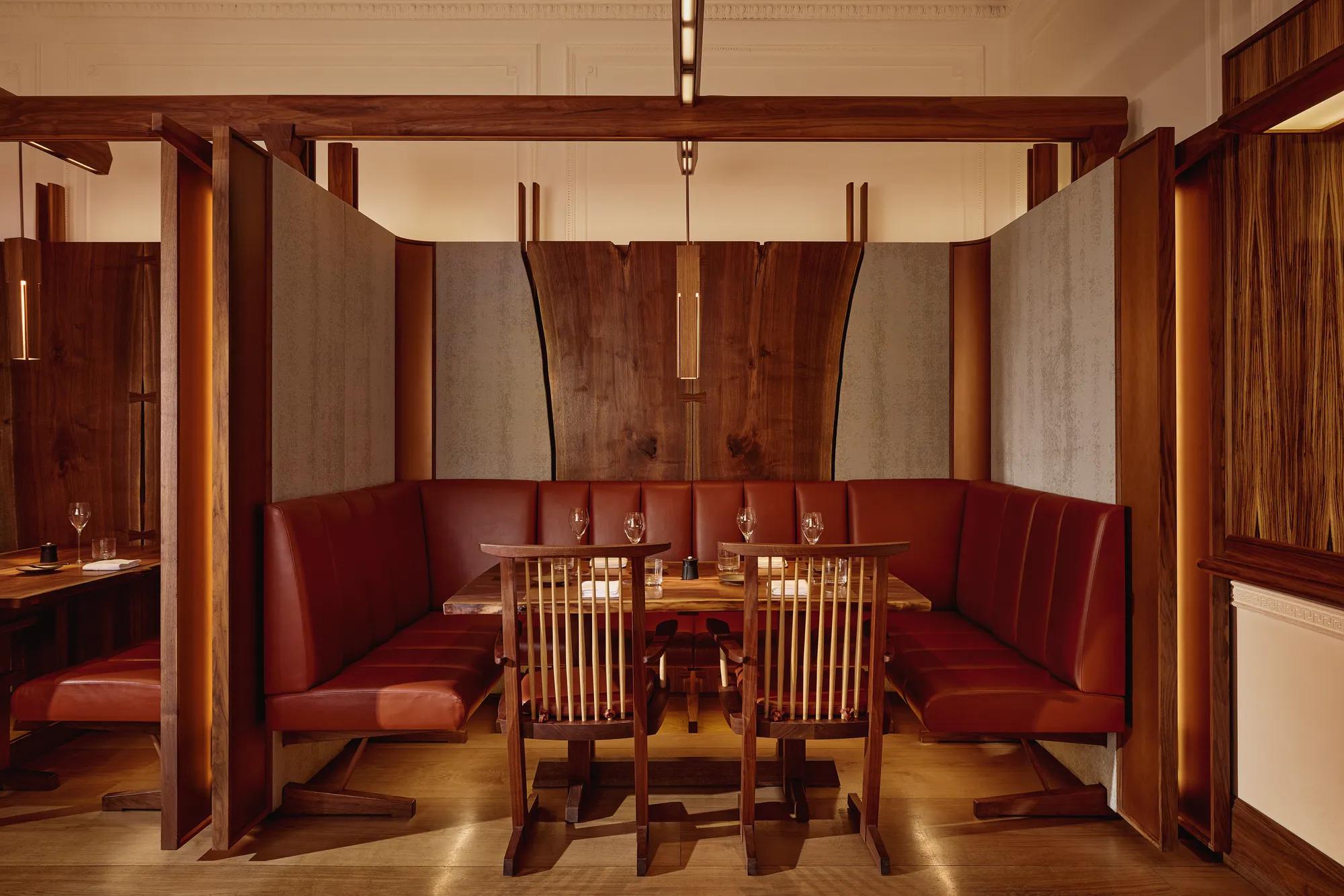 Intimate dining booth with deep red leather seating, wood panelling, and soft pendant lighting.