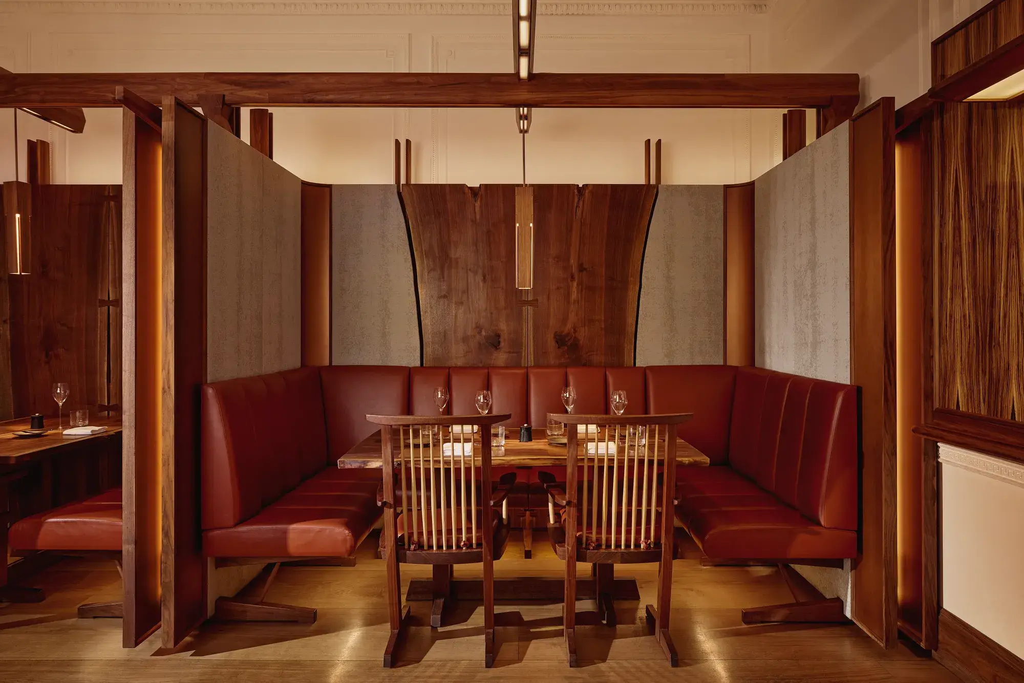 Intimate dining booth with deep red leather seating, wood panelling, and soft pendant lighting.