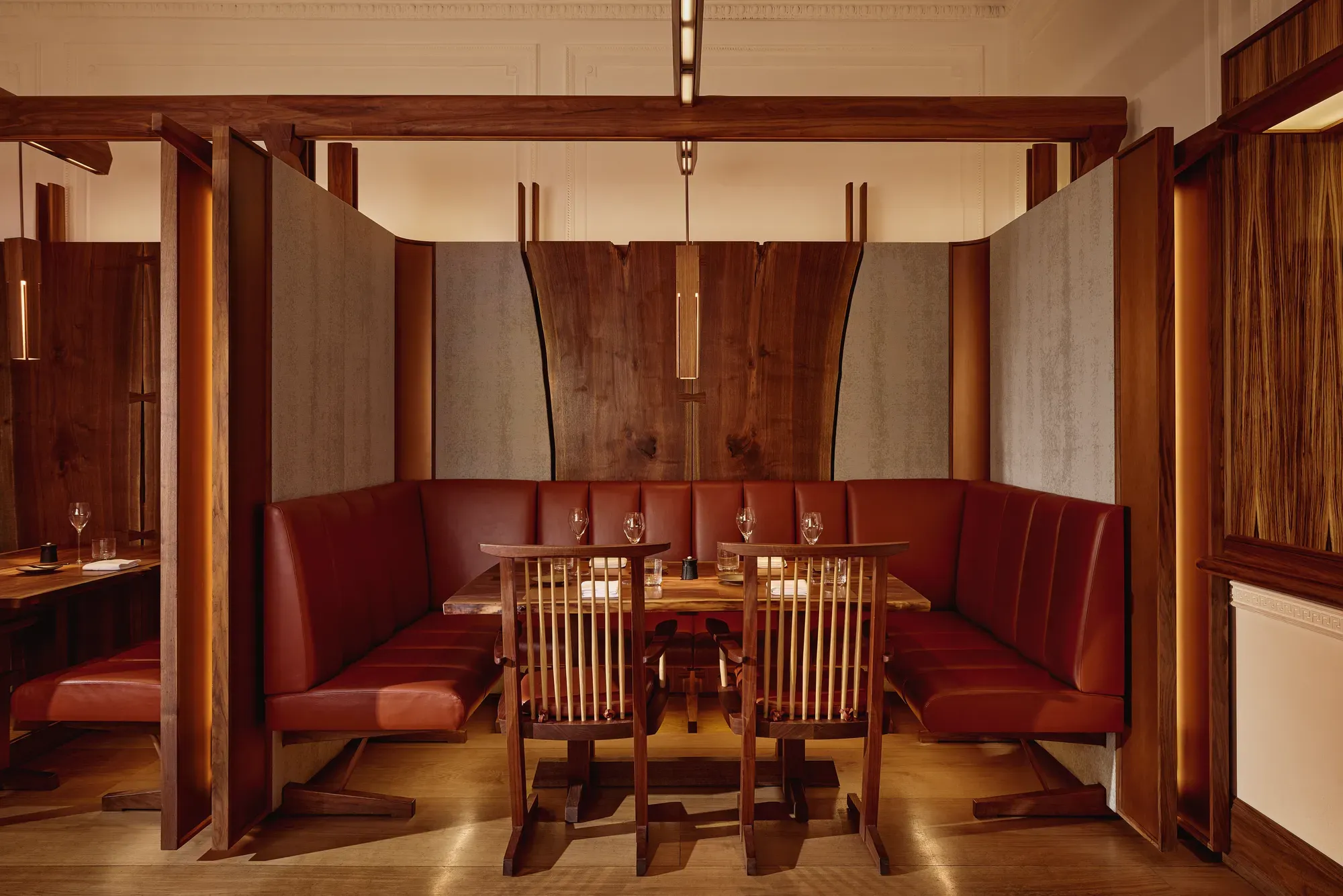 Intimate dining booth with deep red leather seating, wood panelling, and soft pendant lighting.