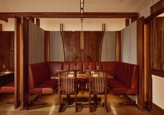 Intimate dining booth with deep red leather seating, wood panelling, and soft pendant lighting.
