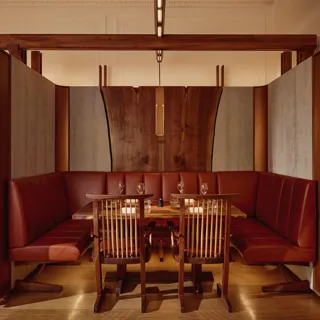 Intimate dining booth with deep red leather seating, wood panelling, and soft pendant lighting.
