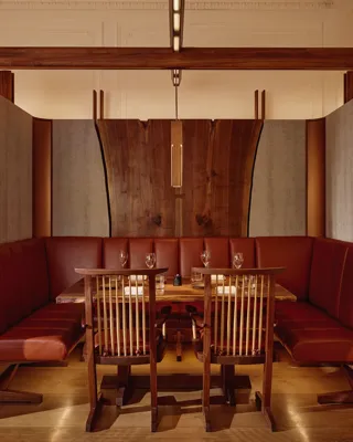 Intimate dining booth with deep red leather seating, wood panelling, and soft pendant lighting.