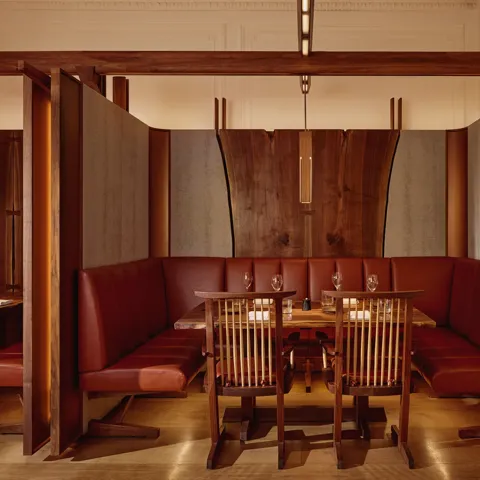 Intimate dining booth with deep red leather seating, wood panelling, and soft pendant lighting.