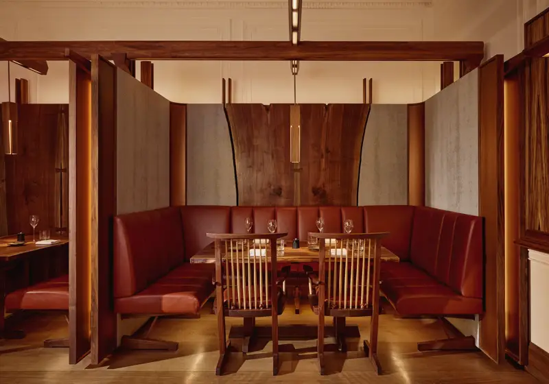 Intimate dining booth with deep red leather seating, wood panelling, and soft pendant lighting.