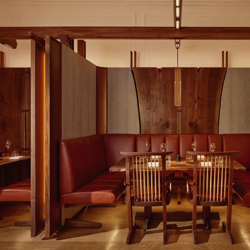 Intimate dining booth with deep red leather seating, wood panelling, and soft pendant lighting.