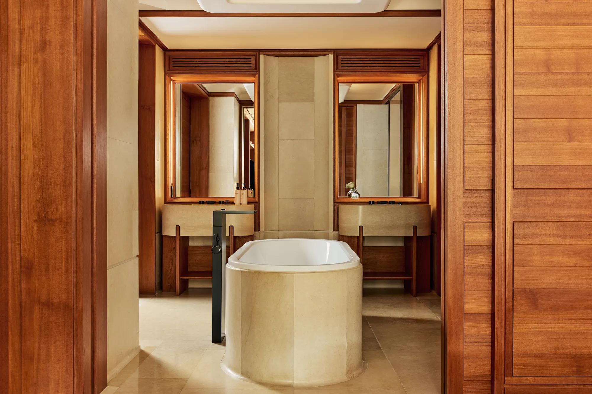 Bathroom with freestanding stone bathtub, twin vanities, and warm wood paneling.
