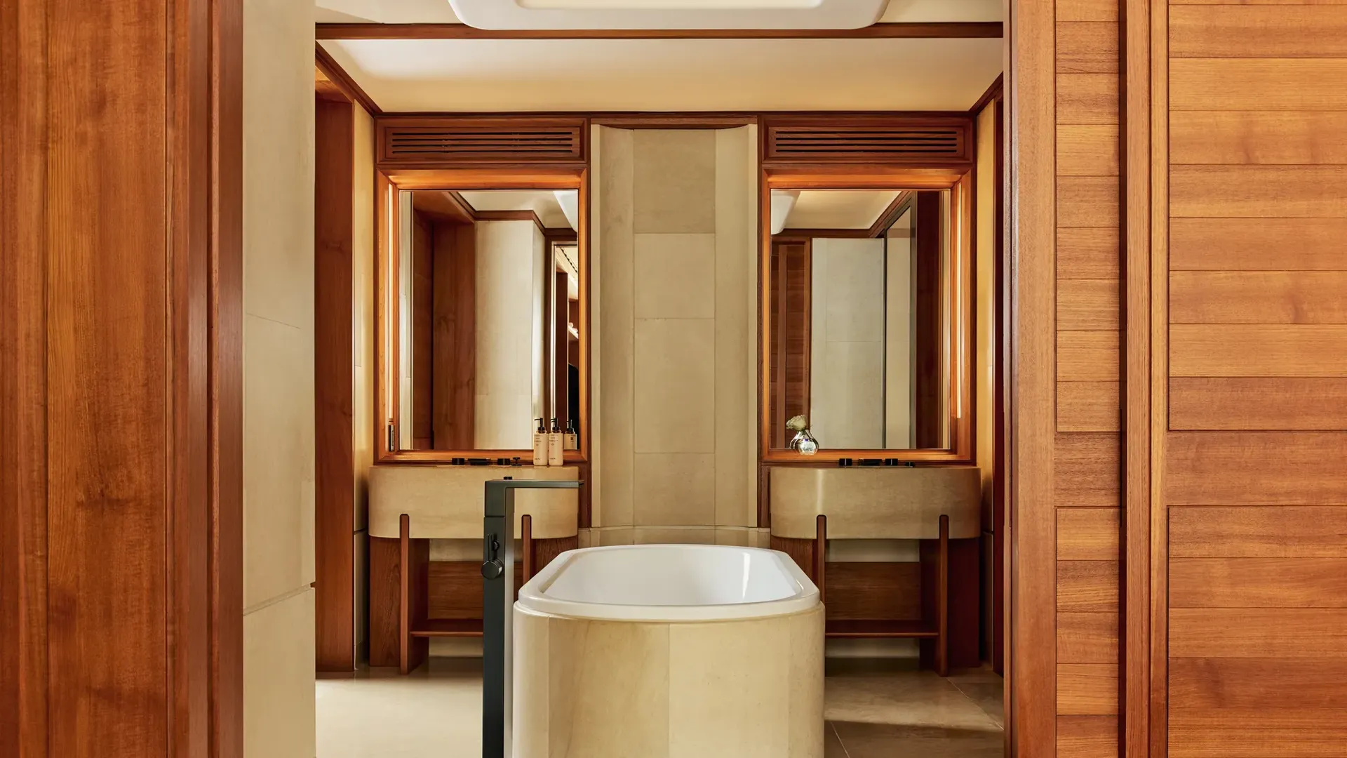 Bathroom with freestanding stone bathtub, twin vanities, and warm wood paneling.