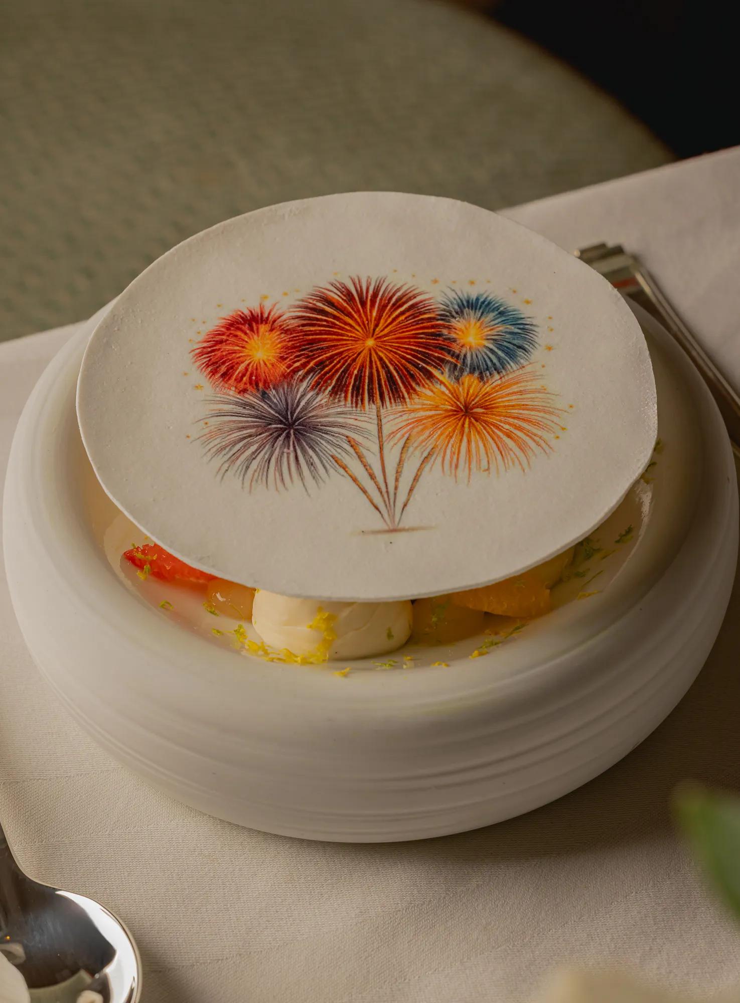 Dessert topped with a decorative wafer printed with colourful fireworks, served in a white bowl.