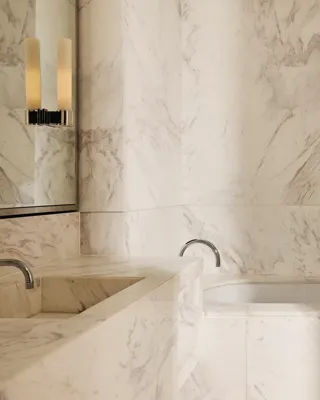 Bathroom clad in white-veined marble, featuring a built-in bathtub, double vanity, and neatly arranged toiletries.