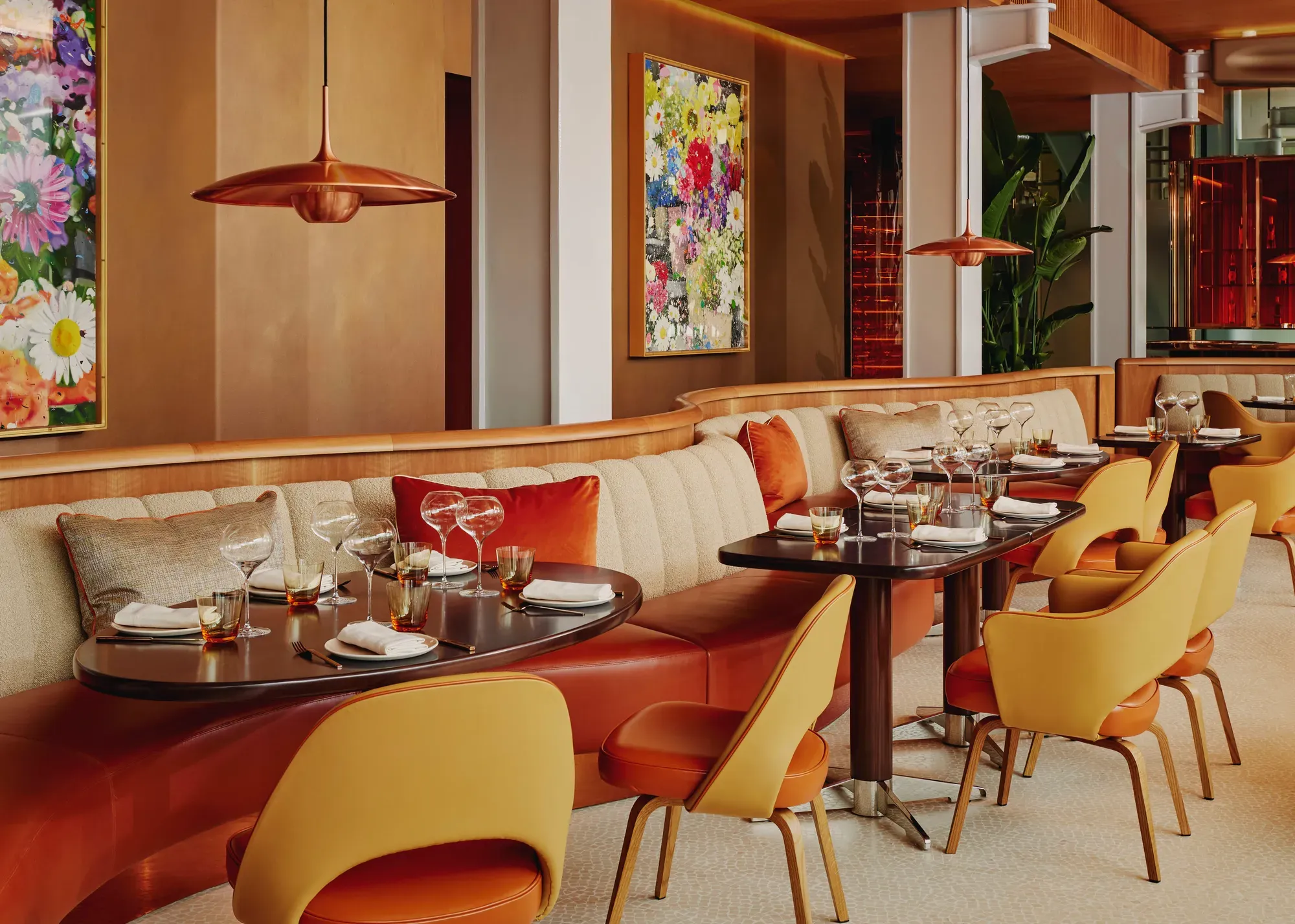 Contemporary restaurant interior with curved banquette seating, amber leather chairs, and tables set for dining in warm lighting.