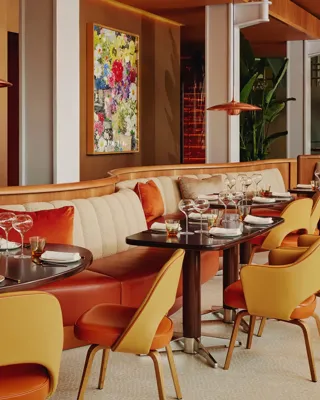 Contemporary restaurant interior with curved banquette seating, amber leather chairs, and tables set for dining in warm lighting.